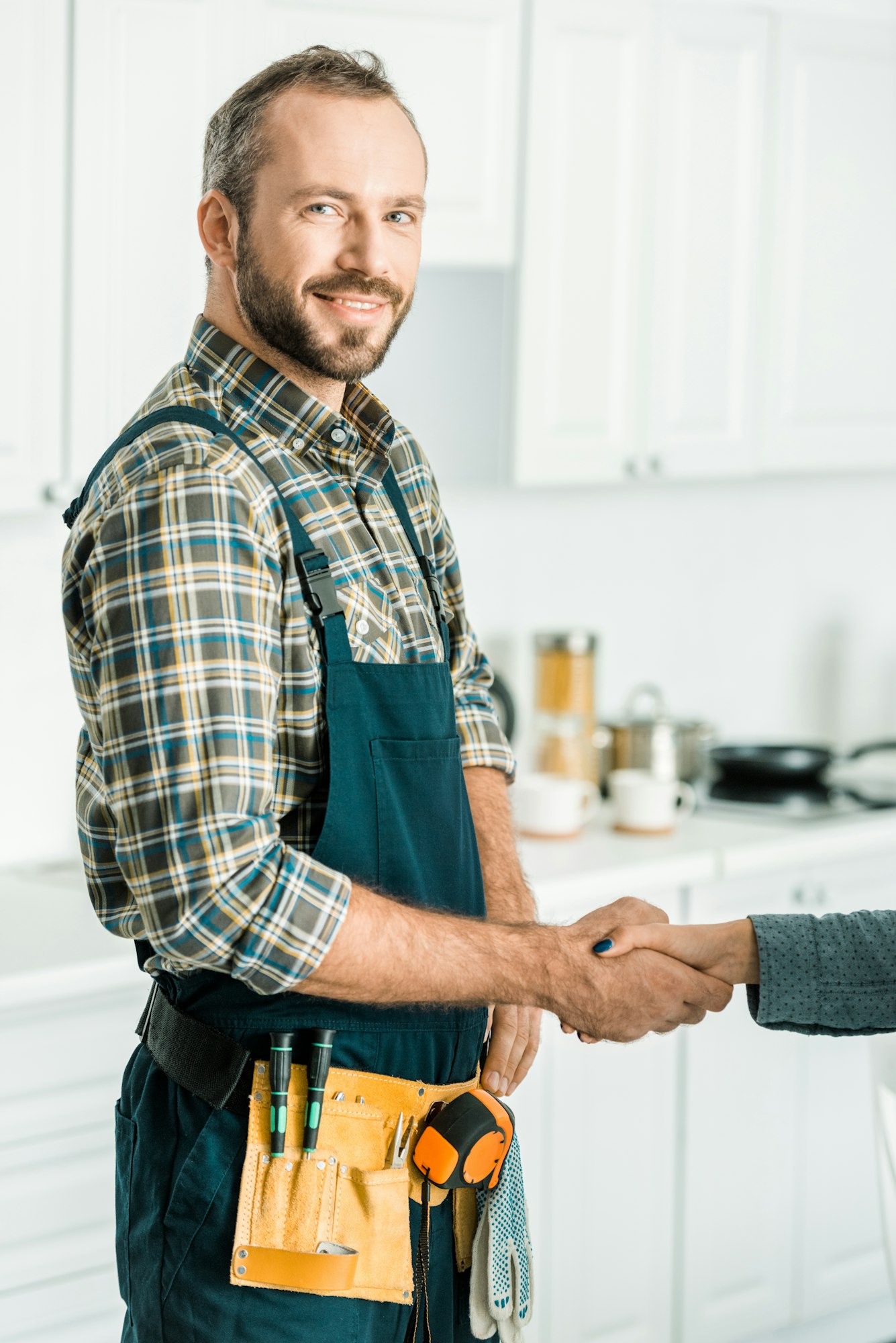 smiling handsome plumber and customer shaking hands in kitchen